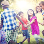 A group of children holding hands and smiling while playing outside.