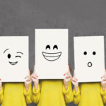 Five people wearing yellow shirts each holding papers with unique emotion in front of their faces.