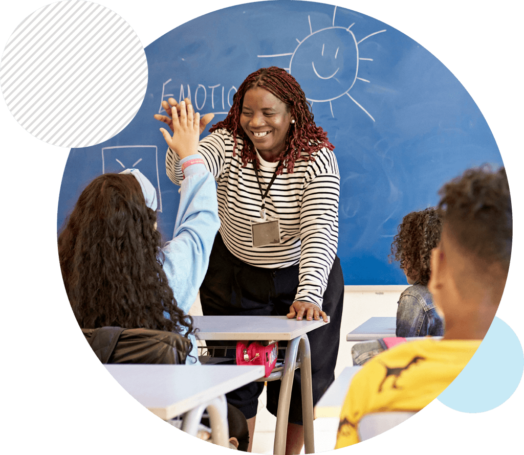 Teacher high-fiving an elementary student who is sitting at a desk at the front of a classroom