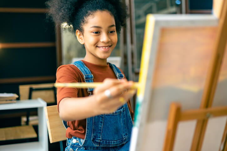 A young teen painting on a canvas.